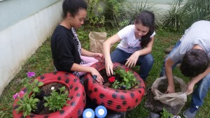 Alunos da COM-VIDA plantando flores em canteiro feito de pneus.
